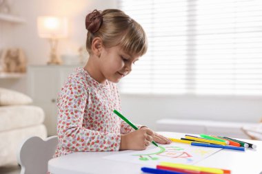 Beyaz masa içinde keçeli kalemle çizen sevimli küçük kız.