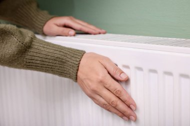 Kadın elini radyatörün yanında ısıtıyor, yakın plan.