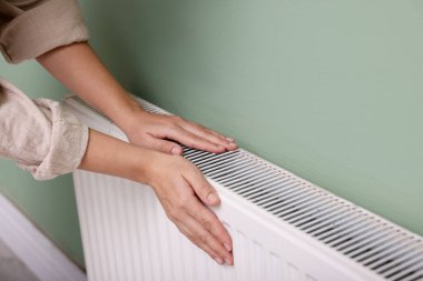 Kadın elini radyatörün yanında ısıtıyor, yakın plan.
