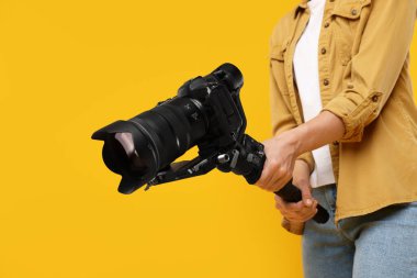 Sarı arkaplanda kameralı titreşim dengeleyici kullanan kameraman, yakın plan