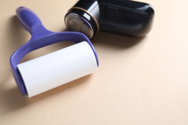 Lint roller and fabric shaver on beige background, closeup. Space for text