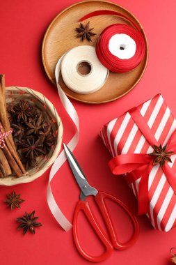 Kutlama ambalajı. Hediye kutusu, kurdele, makas, ambalaj kağıdı ve kırmızı arka planda Noel dekoru, düz yatış