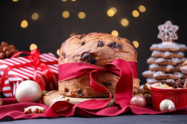 Noel yemeği. Lezzetli Panettone keki, zencefilli kurabiyeler, şekerli meyveler ve siyah ahşap masa üzerindeki dekor bulanık ışıklara karşı, yakın çekim. Bokeh etkisi