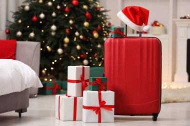 Christmas vacation. Suitcase with Santa hat and gift boxes indoors