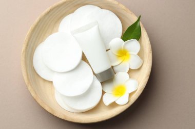 Temiz pamuk pedleri, tesisat çiçekleri ve bej arka planda ahşap kasede kozmetik ürünler tübü.