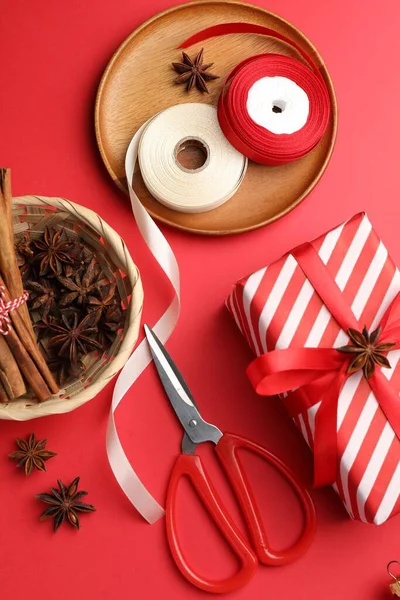 Kutlama ambalajı. Hediye kutusu, kurdele, makas, ambalaj kağıdı ve kırmızı arka planda Noel dekoru, düz yatış