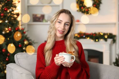 Odada Noel ağacının yanında bir fincan kakaolu güzel bir kadın var.