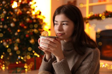 Odada Noel ağacının yanında bir fincan kakaolu güzel bir kadın var.