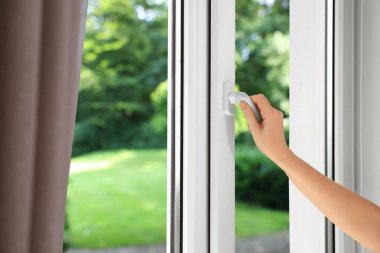 Kadın pencereyi kapatıyor, kapatıyor. Yeşil bahçe, camdan manzara