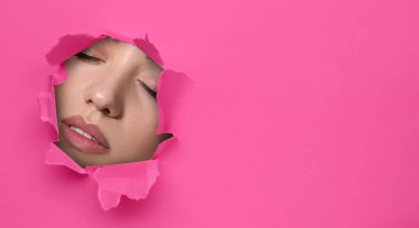 Güzel makyajlı genç bir kadın, yakın plan. Pembe kağıttaki yırtık delikten yüzünü göster