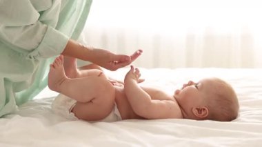 Anne evde bebeğinin vücuduna krem sürüyor, yakın plan.