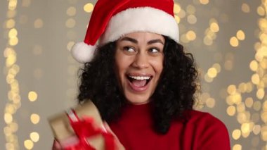 Bulanık ışıklara karşı Noel Baba şapkalı ve Noel hediyeli çekici kadın.