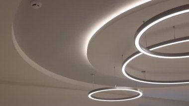 Beyaz tavan lambaları içeriden aydınlatılıyor, yakın plan. Kamera sağa hareket ediyor