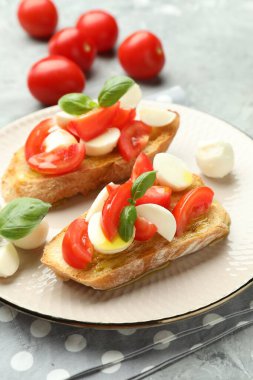 Mozarella peynirli, domatesli ve fesleğenli lezzetli bruschettalar. Gri desenli masa, yakın plan.