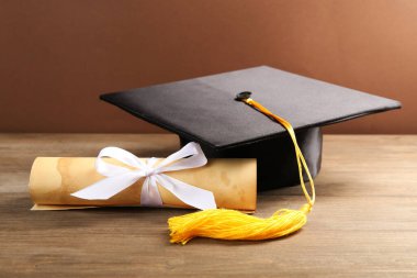 Mezuniyet şapkası ve diploması ahşap masada, kahverengi arka planda, yakın plan.
