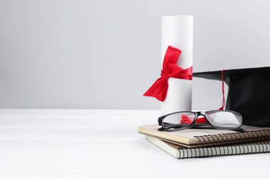Mezuniyet şapkası, diploma, defterler ve gözlük beyaz ahşap masa ve arka planda. Metin için boşluk