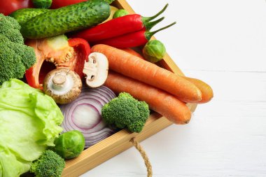Beyaz ahşap masadaki sandıkta farklı taze taze sebzeler, yakın plan.