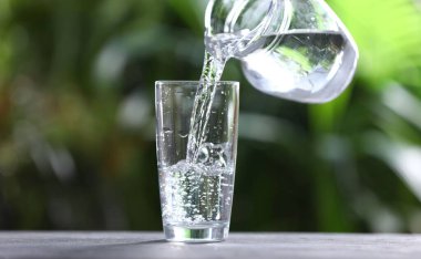 Bulanık yeşil arkaplan, yakın plan, gri masadaki sürahide bardaklara su dökme