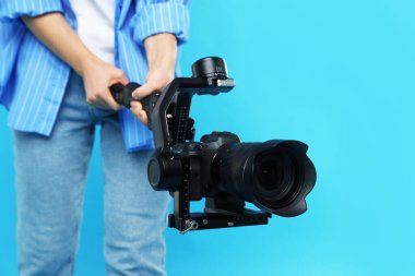 Açık mavi arkaplanda kamerası olan titreşimli dengeleyici kullanan kameraman, kapat