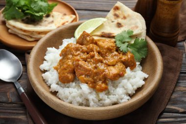 Pirinçli tavuk tikka masala, kişniş, kireç ve lavaş ahşap masada, yakın plan.