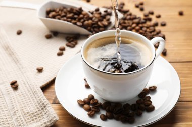 Ahşap masada fincana aromatik kahve ve fasulye dök, yakın plan.