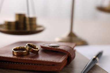 Nafaka. Alyanslar, cüzdan, kalem, terazi ve bozuk paralar ahşap masada, yakın plan.