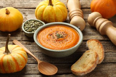 Lezzetli kabak kremalı çorba kasede tohumlar, kızarmış ekmek, sebzeler, değirmenler ve ahşap masada kaşık, yakın plan.