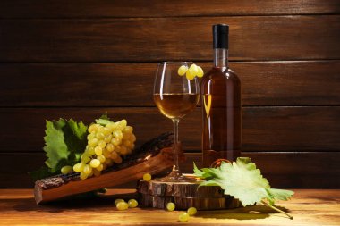 Lezzetli beyaz şarap, cam, şişe, üzüm ve yapraklar ahşap masada.