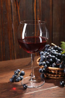Bardakta kırmızı şarap ve ahşap masada üzümler, yakın plan.