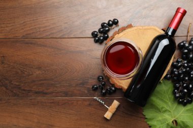 Bardakta kırmızı şarap, şişe, tirbuşon ve tahta masada üzümler, düz yatak. Metin için boşluk