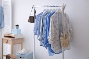 Beyaz duvarın yanında askıda asılı farklı şık kıyafetler, çantalar ve ayakkabılar.