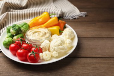 Farklı taze sebzeler ve ahşap masadaki sos, yakın plan.