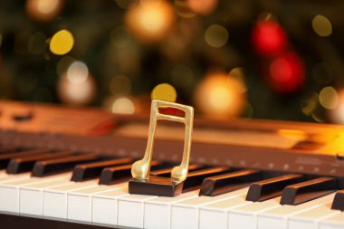 Piyanonun üzerindeki altın müzik notası bulanık Noel ışıklarına karşı, yakın plan. Bokeh etkisi