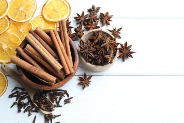 Kâselerdeki farklı baharatlar ve beyaz ahşap masadaki kuru portakal dilimleri düz. Metin için boşluk
