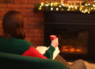 Evde şöminenin yanında kahve kitabı okuyan bir kadın, mesaj atmak için yer var.