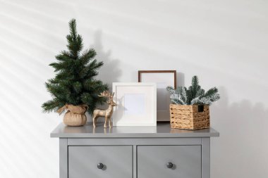 Beyaz duvarın yanındaki gri dolapta farklı Noel dekorları ve çerçeveler var.