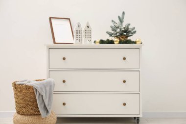 Beyaz duvarın yanındaki dolapta Noel süsü ve çerçeve var.