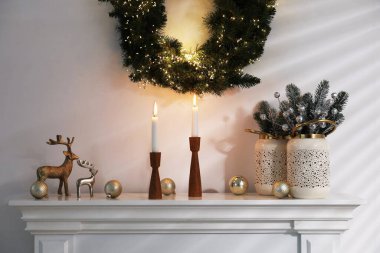 Beyaz duvarın yanındaki şöminede Noel süsü ve yanan mumlar.