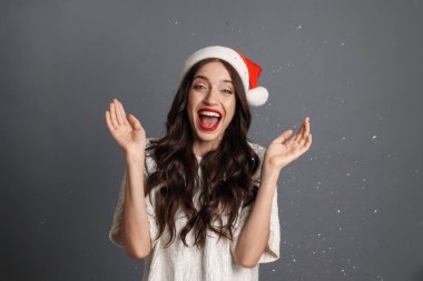 Düşen konfetiyle gri arka planda Noel Baba şapkası takan mutlu kadın. Noel partisi