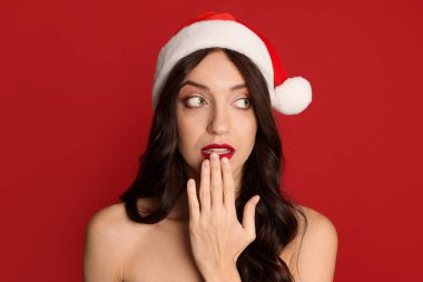 Kırmızı arka planda Noel Baba şapkası olan sürpriz bir kadın. Noel sezonu