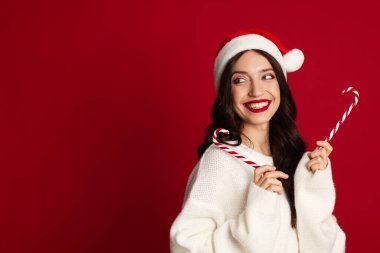 Kırmızı arka planda Noel Baba şapkası ve şeker kamışı olan güzel bir kadın. Mesaj için yer var. Noel sezonu