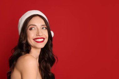 Kırmızı arka planda Noel Baba şapkalı güzel bir kadın, mesaj için yer var. Noel sezonu