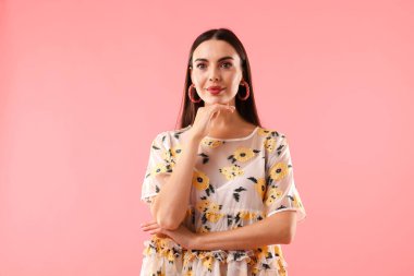 Pembe arka planda poz veren güzel giyimli bir kadın.