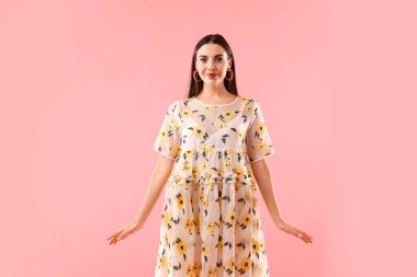 Pembe arka planda poz veren güzel giyimli bir kadın.