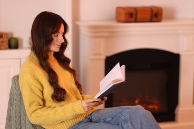 Evdeki şöminenin yanındaki koltukta kitap okuyan kadın, mesaj yazmak için yer.