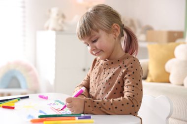 Beyaz masa içinde keçeli kalemle çizen sevimli küçük kız.