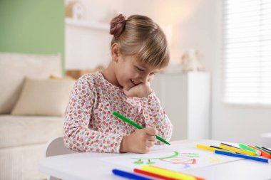 Beyaz masa içinde keçeli kalemle çizen sevimli küçük kız.