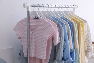 Beyaz duvarın yanında askıda asılı farklı şık kıyafetler, yakın plan.