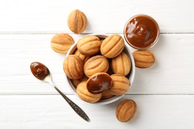 Lezzetli fındık şekilli kurabiyeler haşlanmış süt ve kaşık beyaz ahşap masada, düz yatıyordu.