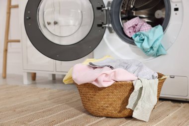 Çamaşır sepetinin içinde çamaşır ve çamaşır makinesi var.